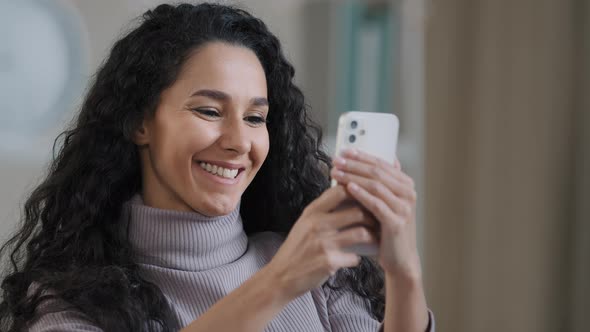 Close Up Portrait of Young Happy Hispanic Woman Holding Phone Browsing Social Networks Smiling alt