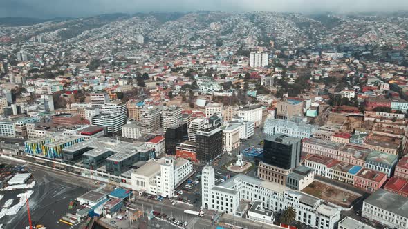Aerial panning of Valparaiso hillside city buildings, sea port, and cars driving near Plaza Sotomayo alt