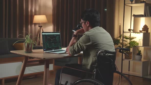 Asian Man Trader Sitting In A Wheelchair While Trading Cryptocurrency On Laptop Computer at Home alt