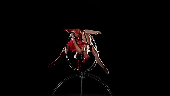 Two Girls Aerialists Spinning on a Hoop on Stage. Black Background. Slow Motion alt