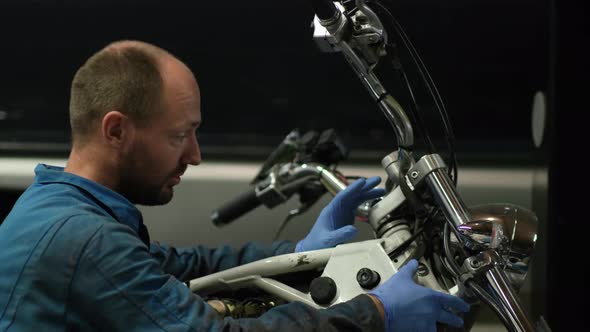 guy mechanic in blue overalls next to a motorcycle