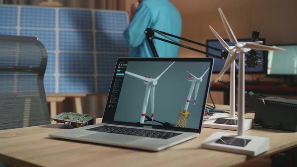 Laptop Showing Wind Turbine On The Table While A Man Walks Into The Office To Look At Solar Cell alt