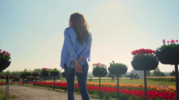 Back View of Relaxed Girl with Camera Walking in Summer Flower Park in Sunshine alt