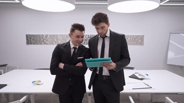 Two Excited Confident Caucasian Men Making Victory Gesture Surfing Internet on Tablet Standing in alt