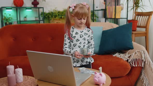 Little Kid Girl Counting Money Dollar Banknotes for Future Needs at Home Desk with Laptop Piggybank alt