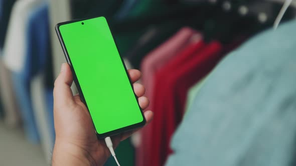 Man in Teal Shirt holds steadily his Mobile Phone while Watching and Listening through the Headphone alt
