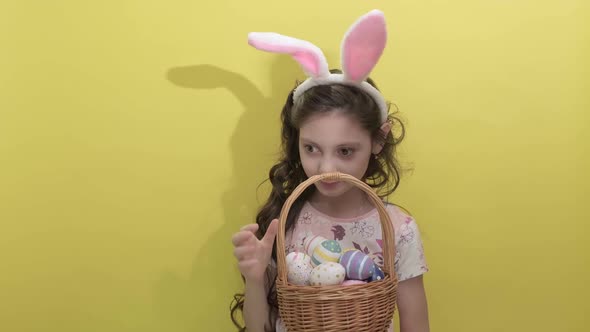 Beautiful Cute Little Girl in Easter Bunny Ears Holds a Basket with Eggs alt