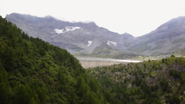 View of a dam in the swiss alps, next to a mountain lake. aerial shot, fir forest alt