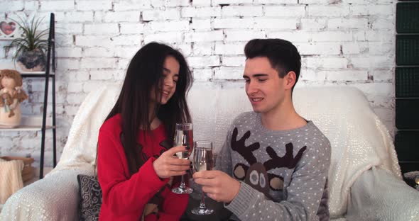 Young Couple Sitting on Sofa Looking at Each Other with Glasses in Hands alt