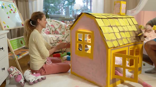 Young Family with Child Building and Painting Toy Cardboard House Together.