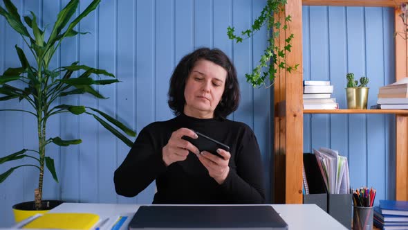 Middle Aged Old Woman Play Mobile Games on Mobile Phone at Home Office