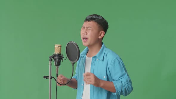 Side View Of Young Asian Boy Singing Into Microphone In Green Screen Studio alt