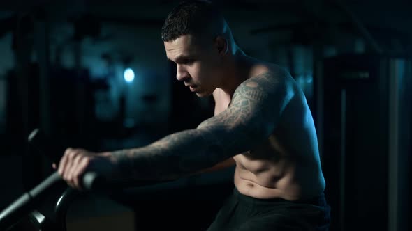 A Handsome Young Muscular Sportsman is Doing Exercise on a Fitness Machine in the Gym