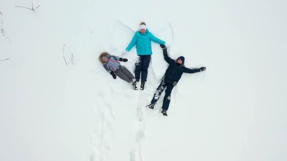 A Family with Children Makes a Figure of a Snow Angel in a Clearing in the Forest alt