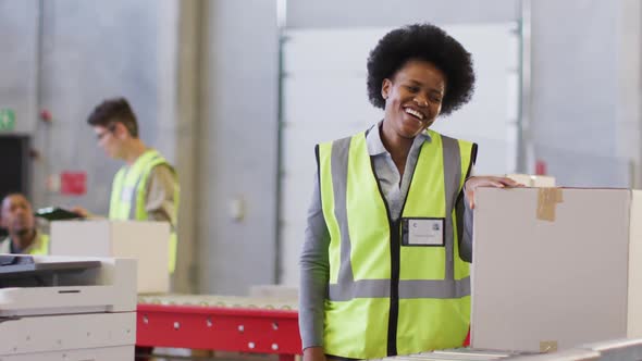Portrait of african american female worker wearing safety suit and smiling in warehouse alt