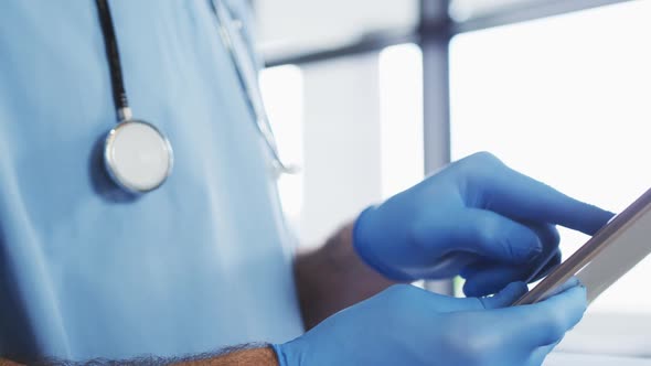 Caucasian male doctor wearing protective gloves using digital tablet alt