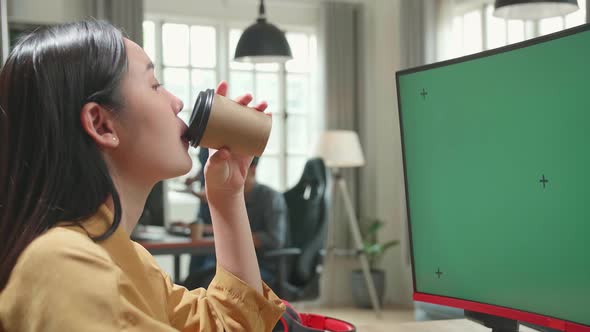 Asian Female Works And Drinking Coffee With Mock Up Green Screen Computer Display In Office alt