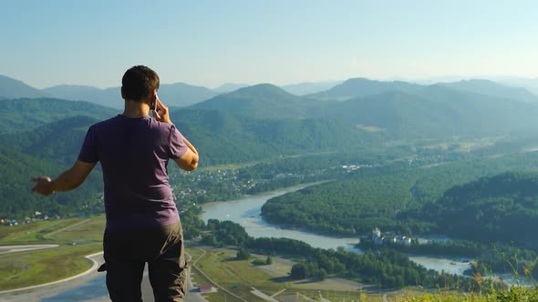 Young Man Is Talking On A Mobile Phone On A Mountain Landscape Background