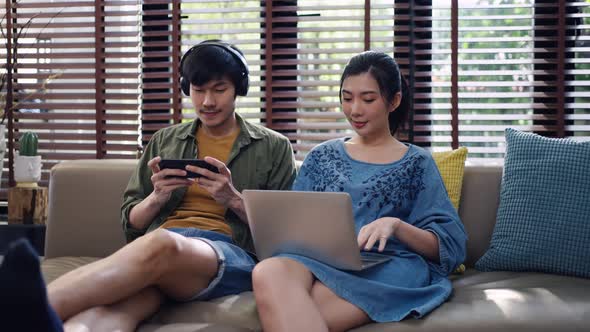 Asian couple using a smartphone and laptop computer in living room.