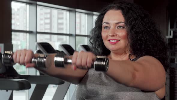 Happy Plus Size Sportswoman Lifting Dumbbells at the Gym alt