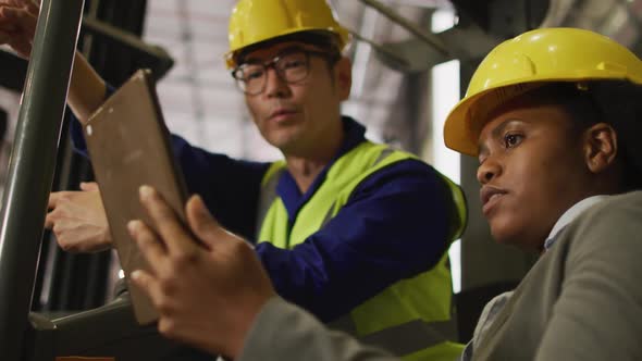 Diverse male and female workers wearing safety suits and using tablet in warehouse alt