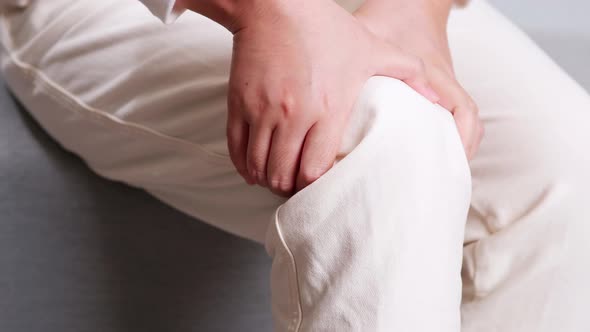 Close up of woman sitting on sofa doing self massage on knee for relieving pain. Medical and healthc alt