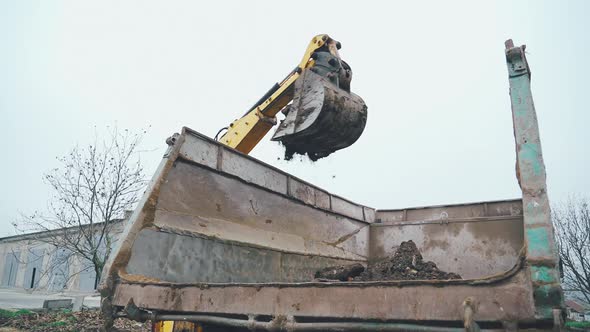 Excavator arm scoops up a bucket full of soil and rocks during roadworks in the countryside. Close u