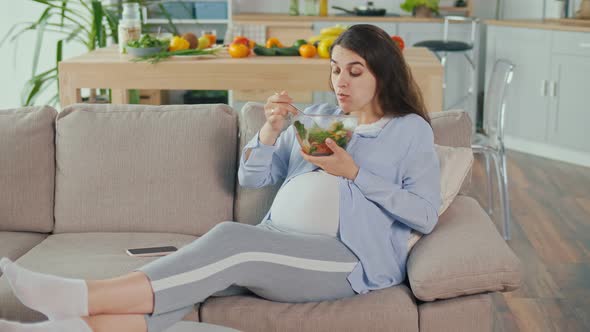 Pregnant Woman With Great Appetite Eats Vegetable Salad Lying on the Sofa alt