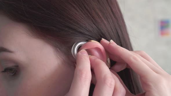 Young Woman Inserts a Hearing Aid Into Her Ear Close Up alt