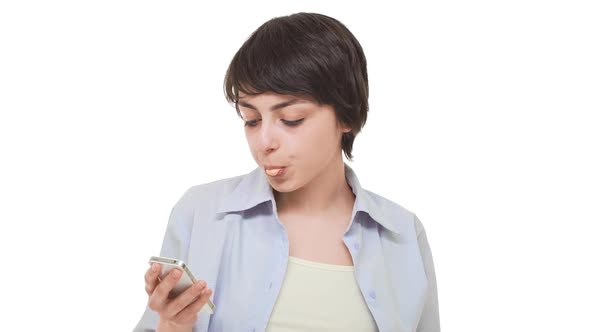Lazy Caucasian Girl with Short Haircut Staring at Cellphone Chewing Gum and Blowing Bubbles alt