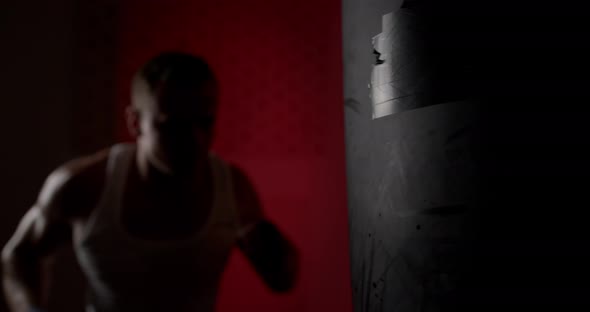 A man in a semi-dark hall, wearing hand wraps, hits a punching bag with quick and accurate punches. alt