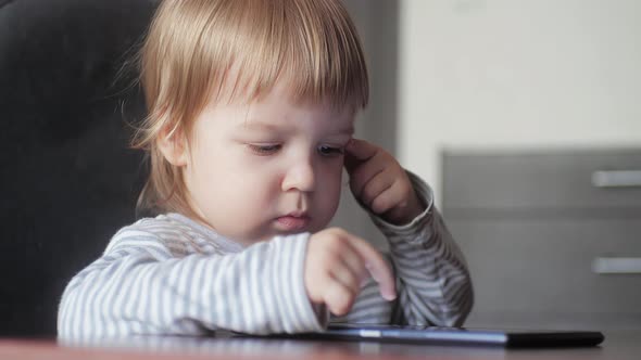 Cute Toddler Boy Using a Digital Device While Sitting at a Desk