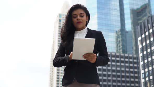 Young Indian businesswoman using digital tablet standing against corporate buildings in the city