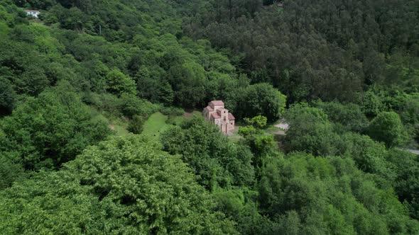 Droone flying towards ancient and roman church in green natural forest environment alt