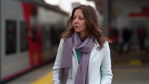 Portrait of a Middle-aged Woman Standing on a Platform on the Street, a Train Passes Behind Her. She alt