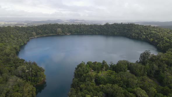 Aerial drone video revealing a large volcanic crater lake fringed with a lush tropical rainforest alt