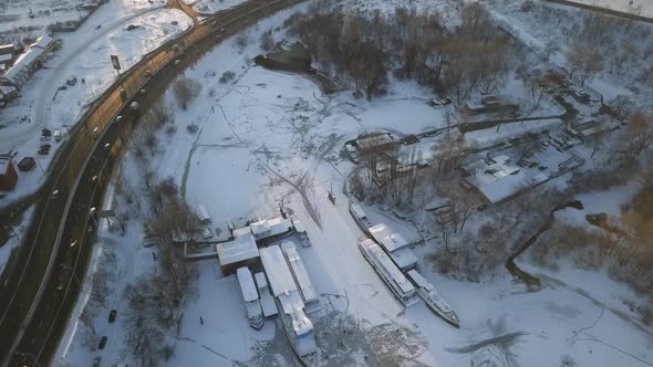 Flying Over a Road with Cars Along the Bay with Frozen Ships During a Winter Sunset and Traces of