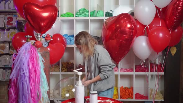 Woman Ties with a Ribbon a Round Transparent Balloon with White Feathers Inside alt