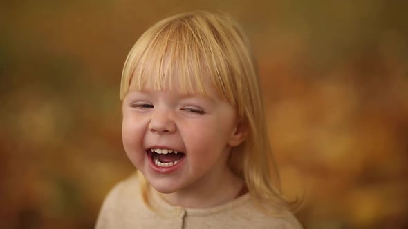 Happy Beautiful Baby Girl with Blonde Hair Laughing in the Autumn Park