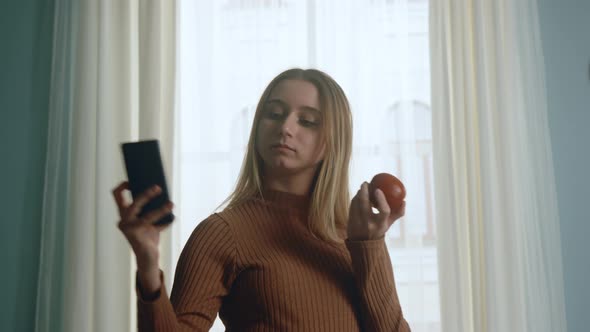 Young Girl with a Red Apple Takes a Selfie on a Cell Phone