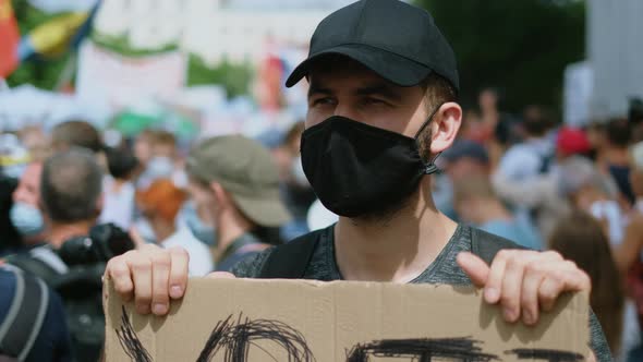Political rally riot activist in face mask with poster sign against coronavirus. alt