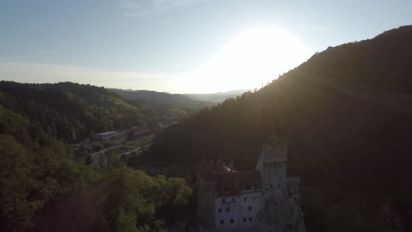 Aerial of sun shining above Bran Castle and hills alt