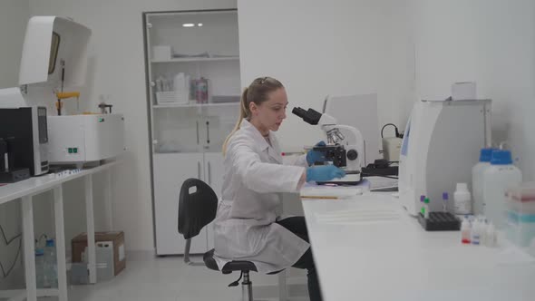 Female Medical Professional Works with Samples and Analyzes in Medical Laboratory Behind Microscope alt