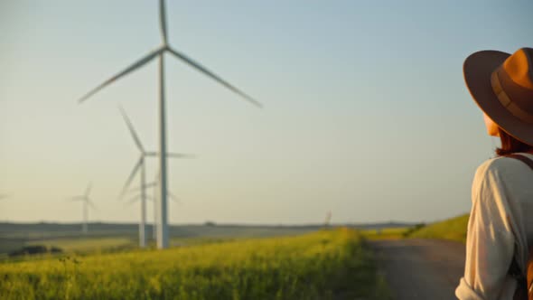 Young tourist in a hat looking at eco windmills in a field alt