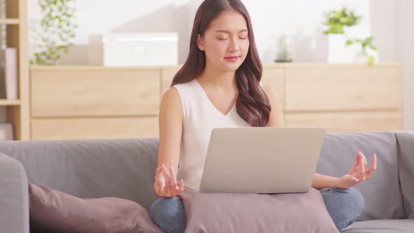 Clam of Asian young woman doing yoga lotus pose to meditation and relax on couch during work online alt