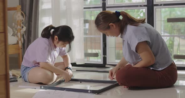 Asian Woman And Daughter Move To New Home Assembling Furniture Together, Daughter Helps Mother. alt
