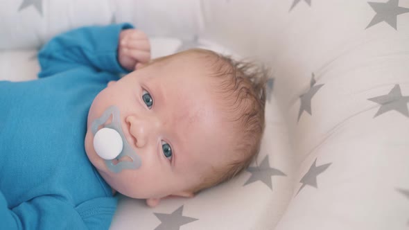 Newborn Boy with Blue Eyes Sucks Dummy in Sleeping Cocoon alt