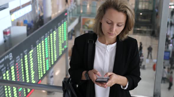 Businesswoman Using Mobile Phone And Checking Time At Smartwatch At Airport. alt