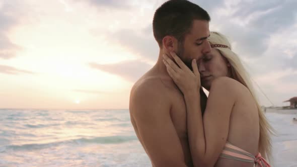 Young Man Woman Couple in Love Hugs and Kisses at Ocean Beach Seaside at Sunrise or Sunset in Summer alt