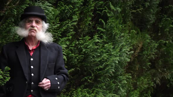 Older man with beard looks at camera through trees, leprechaun concept alt